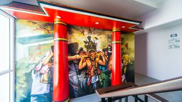 A mural with a group of people, a staircase with red pillars, and a window with a view of the outdoors.