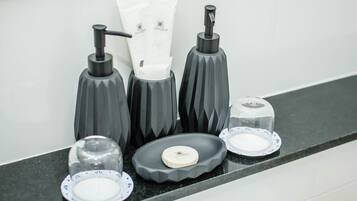 A bathroom counter with a soap dispenser, a tissue dispenser, a soap dish, and a glass soap dish.