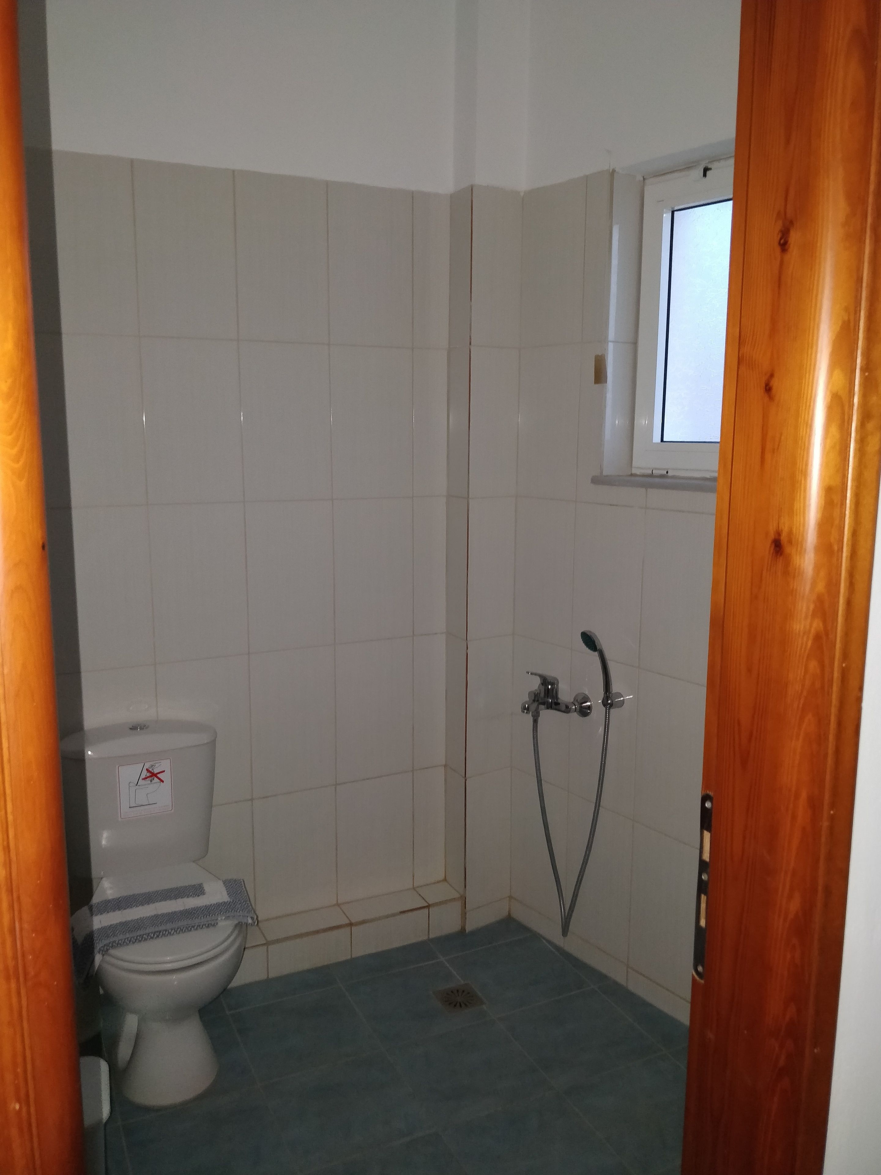 A small bathroom with a toilet, a shower, and a window.