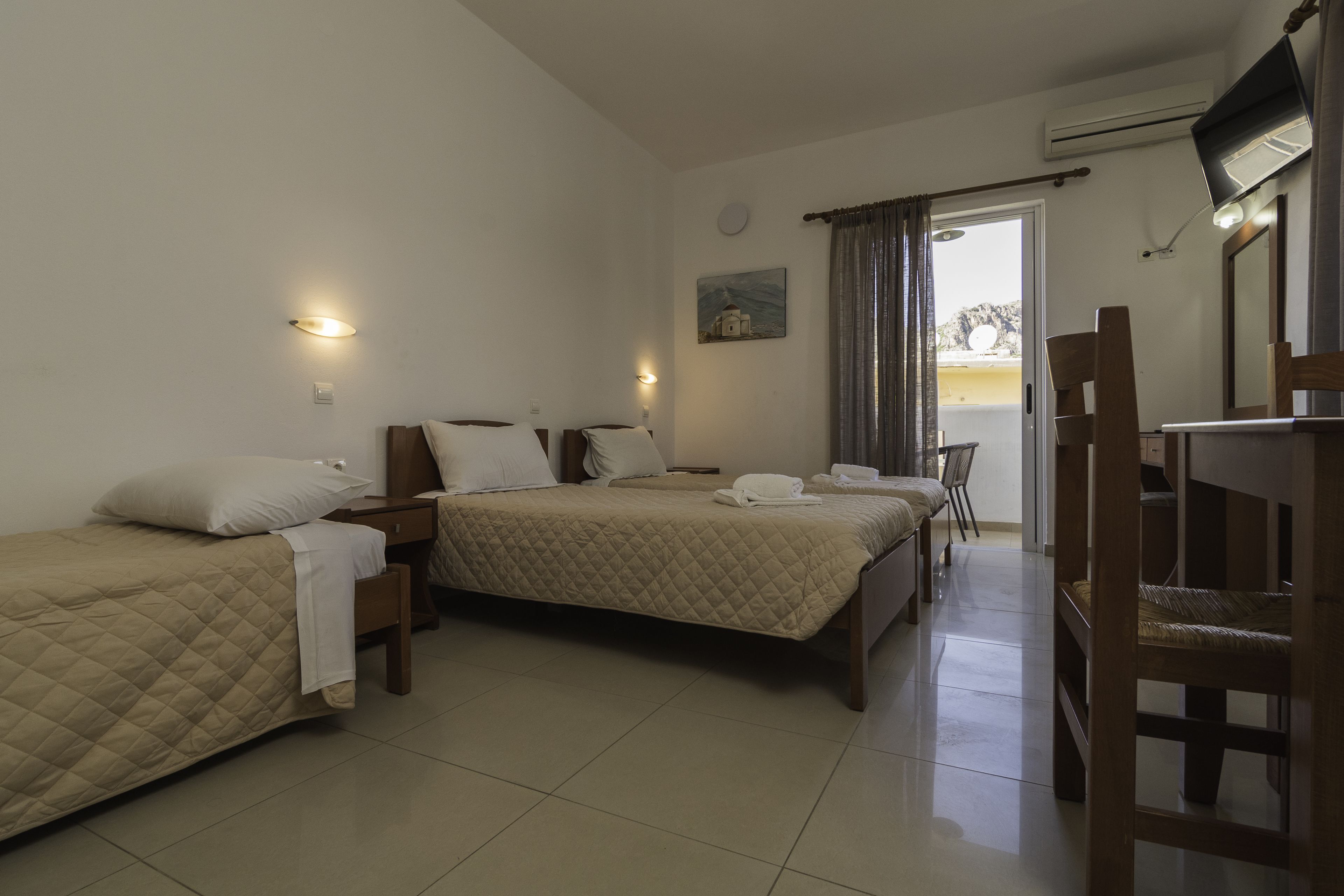A hotel room with two beds, a desk, a chair, and a TV.