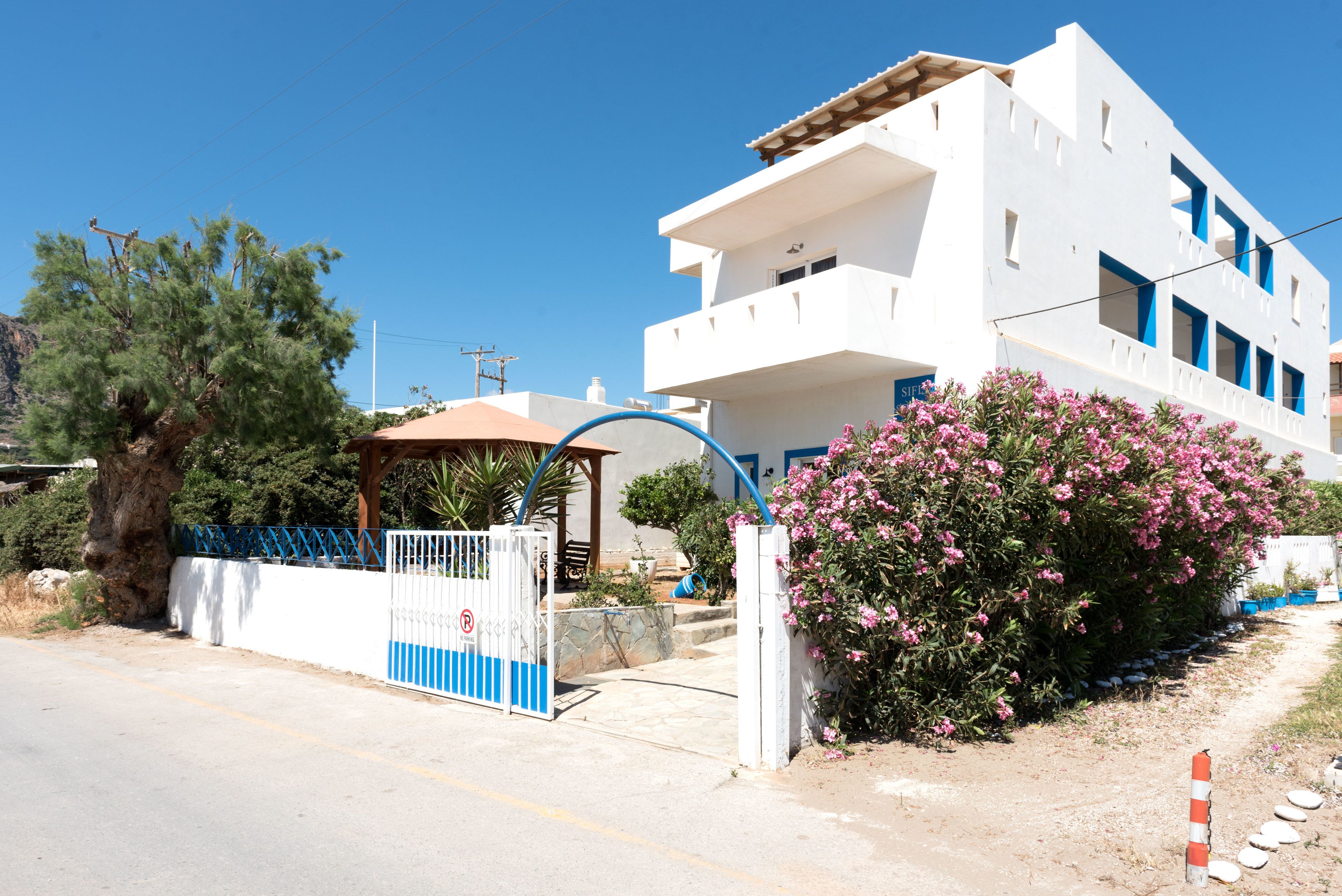 Un bâtiment blanc avec une porte bleue et une entrée fermée par un portail.