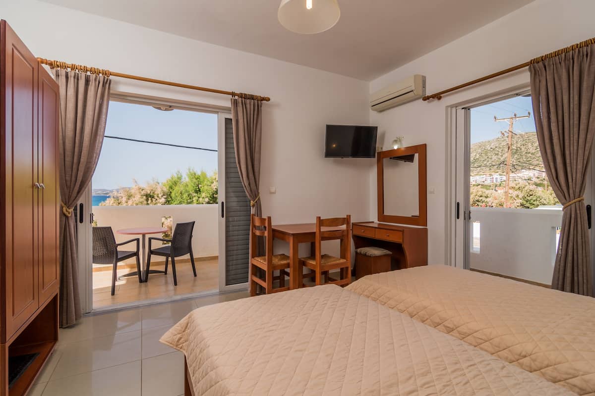 Une chambre d’hôtel avec un lit, un bureau, une chaise, une télévision et un balcon avec des rideaux.