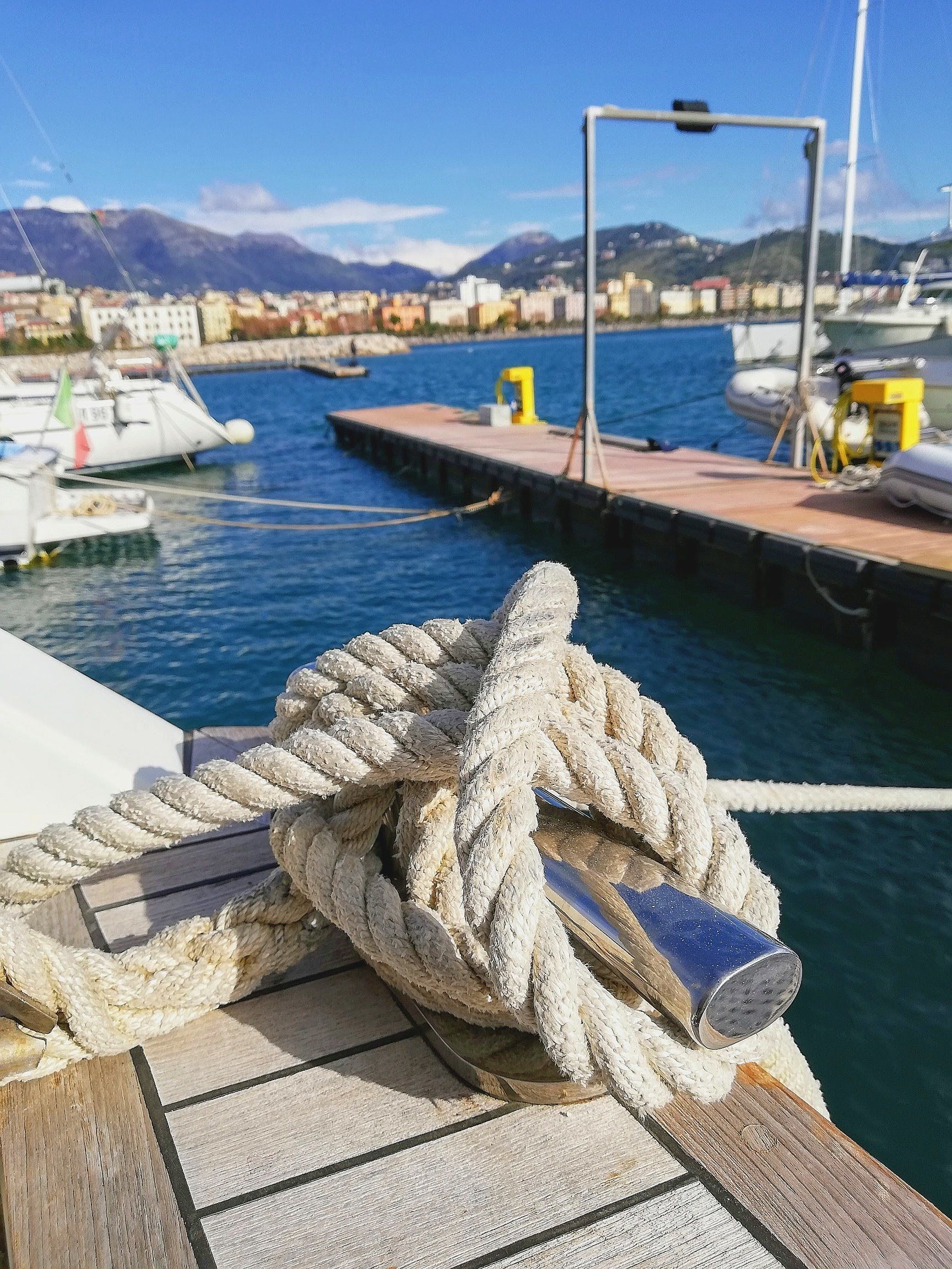 A close-up of a rope on a dock with boats in the background.