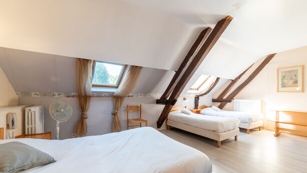 A bedroom with a large bed, two smaller beds, a chair, a desk, a radiator, a fan, and a window with curtains. - Hôtel Du Cygne (Auxerre)