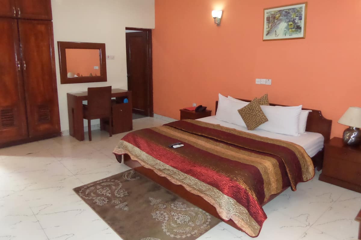 A hotel room with a bed, a desk, a chair, a wardrobe, and a painting on the wall.