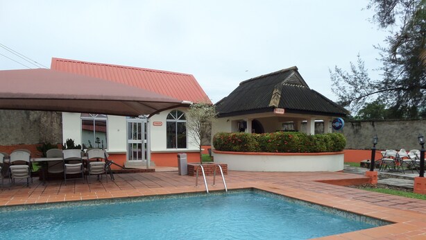 A swimming pool with a tiled deck, outdoor seating, and a building with a red roof and signage. - The Town House (Ibadan)