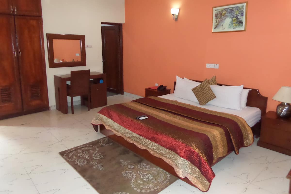 A hotel room with a bed, a desk, a chair, a wardrobe, and a painting on the wall.