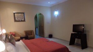 A hotel room with a bed, a TV on a stand, a chair, a desk, and a picture on the wall. - The Town House (Ibadan)