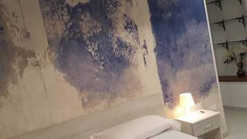 Une chambre à coucher avec un lit, des oreillers blancs, une table de chevet avec une lampe et un mur orné d’un motif texturé.