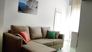 Un salon avec un canapé marron, un coussin rouge et vert, et un tableau encadré accroché au mur.