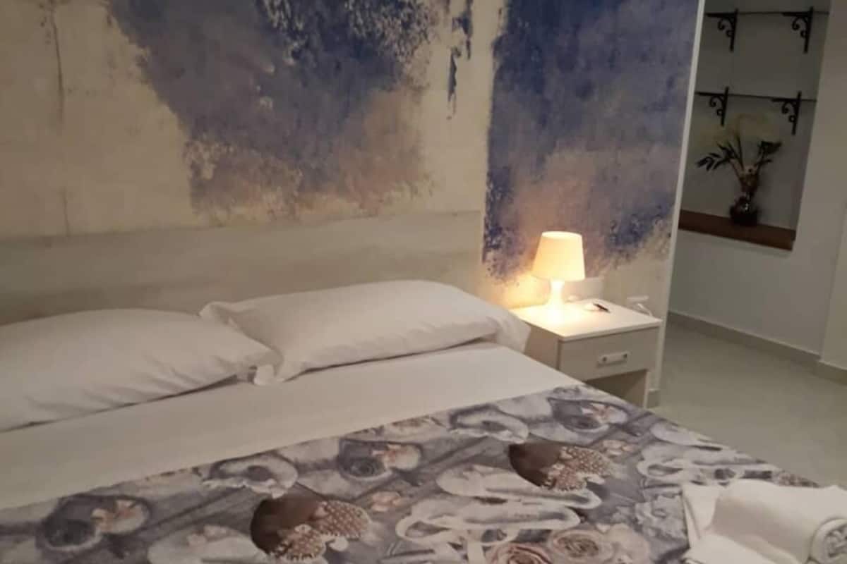 Et soveværelse med seng, puder, et natbord med lampe, og væg med dekorativt mønster.