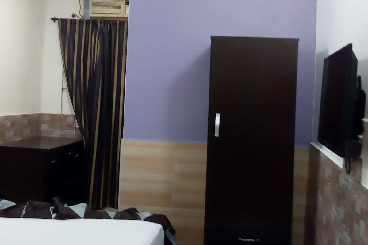 Una habitación de hotel con cama, armario, refrigerador pequeño y ventilador de techo.