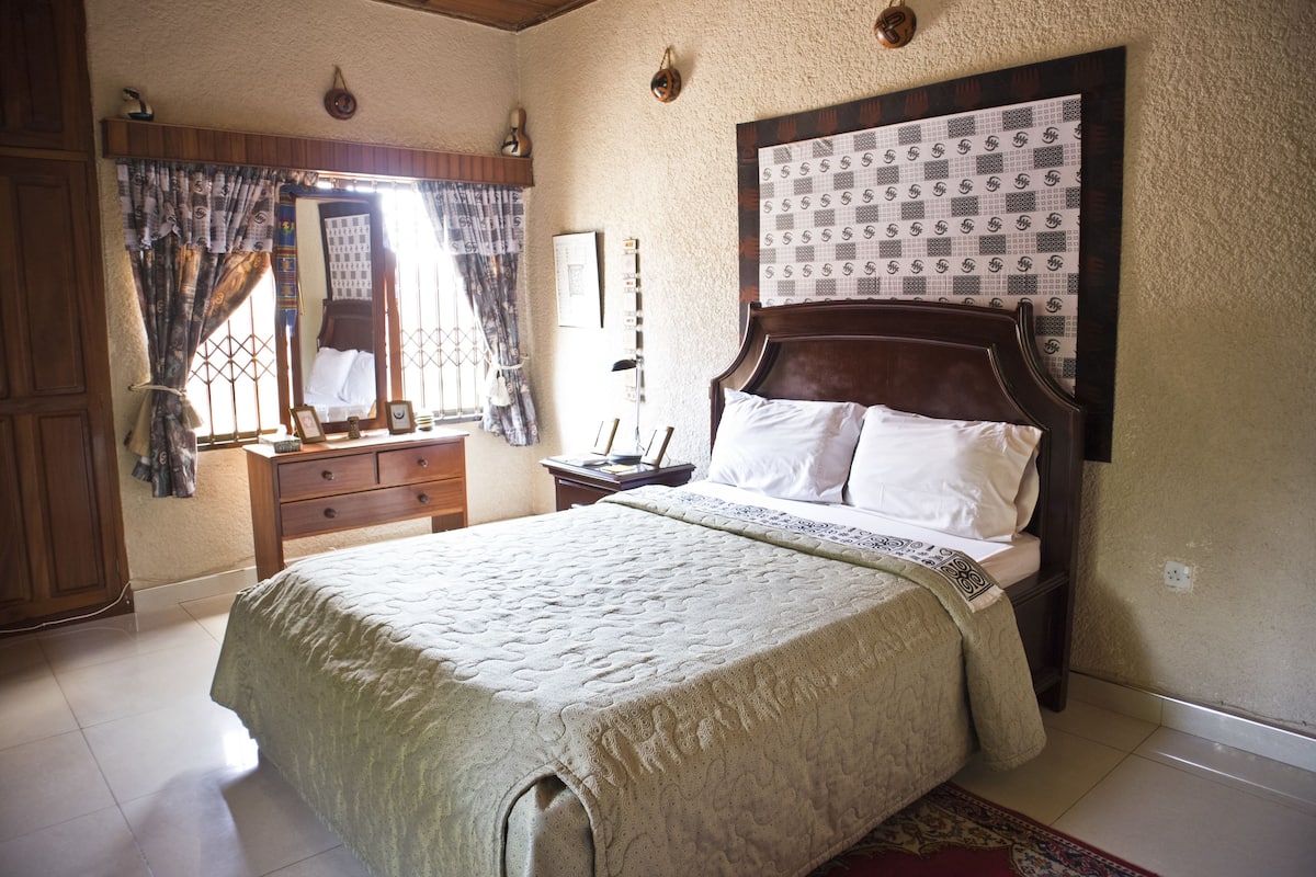 A bedroom with a large bed, a dresser, a mirror, and a patterned headboard.