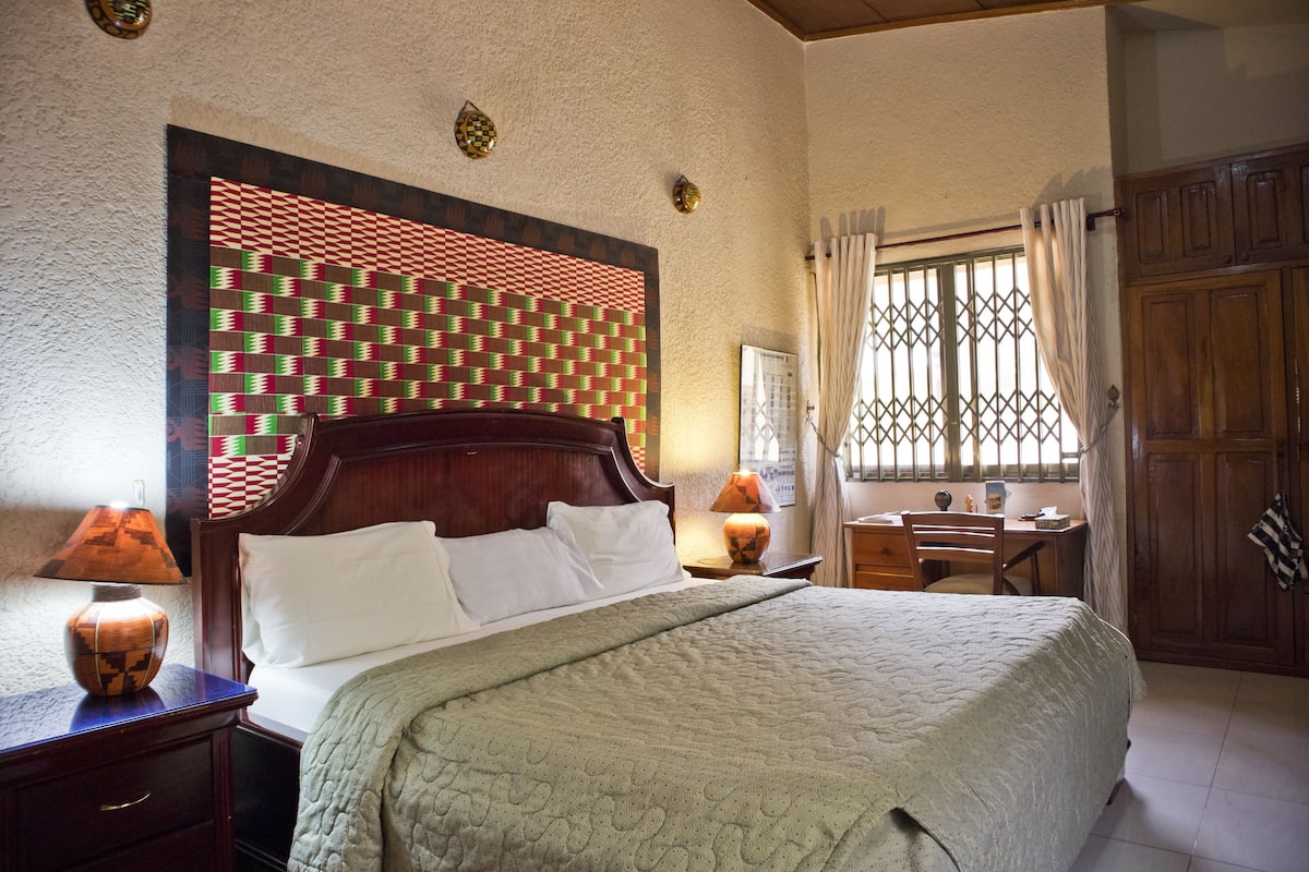 A bedroom with a wooden bed, a desk, and a window with bars.
