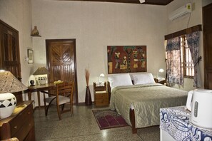 Une chambre à coucher avec un lit, une chaise, une table, une lampe, un tableau et une fenêtre avec des rideaux.