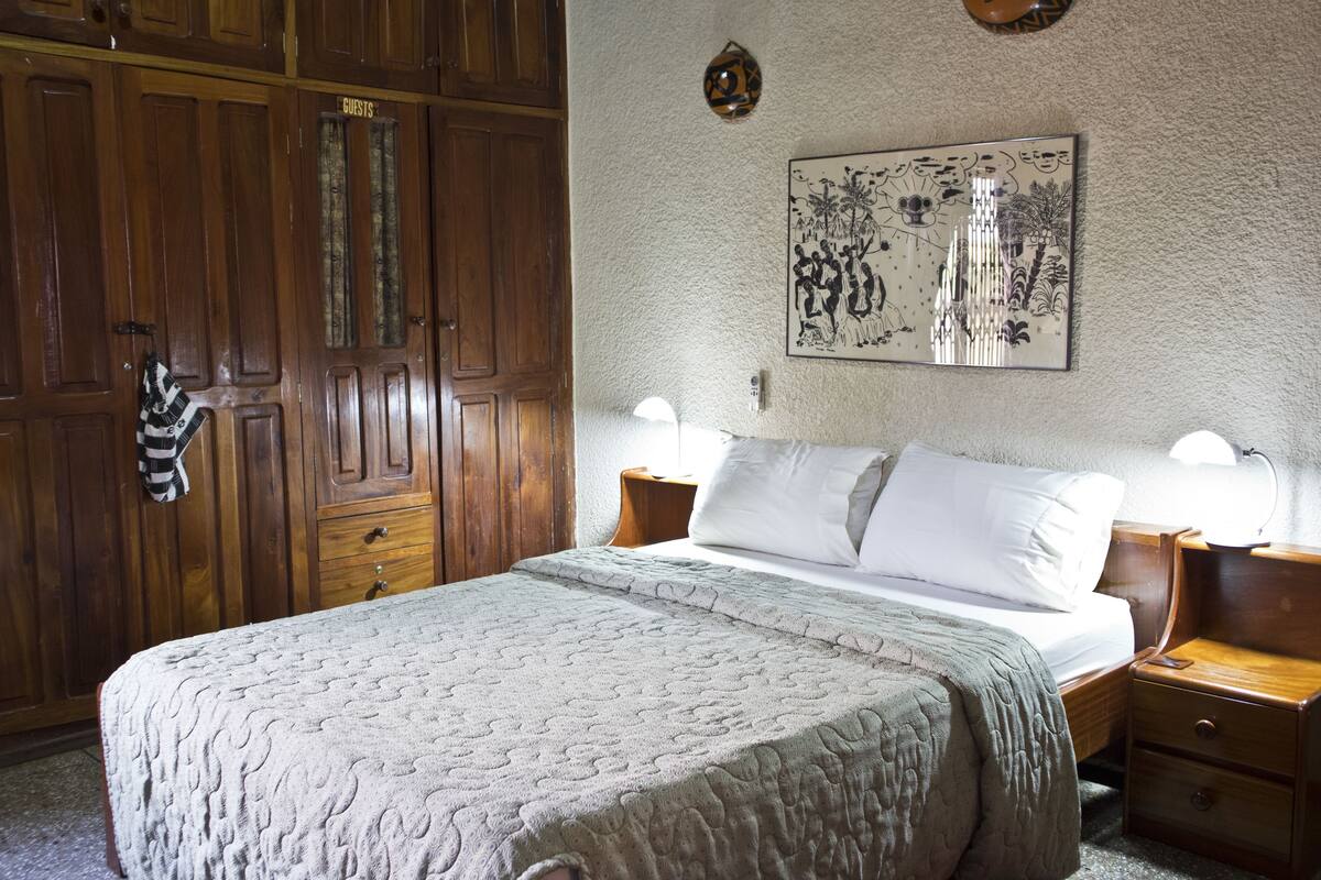 A neatly made bed with a quilt, wooden nightstands, a wall-mounted lamp, and a door labeled "Guests".