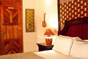 Une chambre d’hôtel avec une porte en bois, une œuvre d’art encadrée, une lampe de style traditionnel et un lit avec des oreillers blancs.