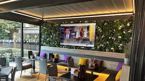 Een moderne zithoek met zitplaatsen en een televisiescherm waarop een nieuwsuitzending draait.
