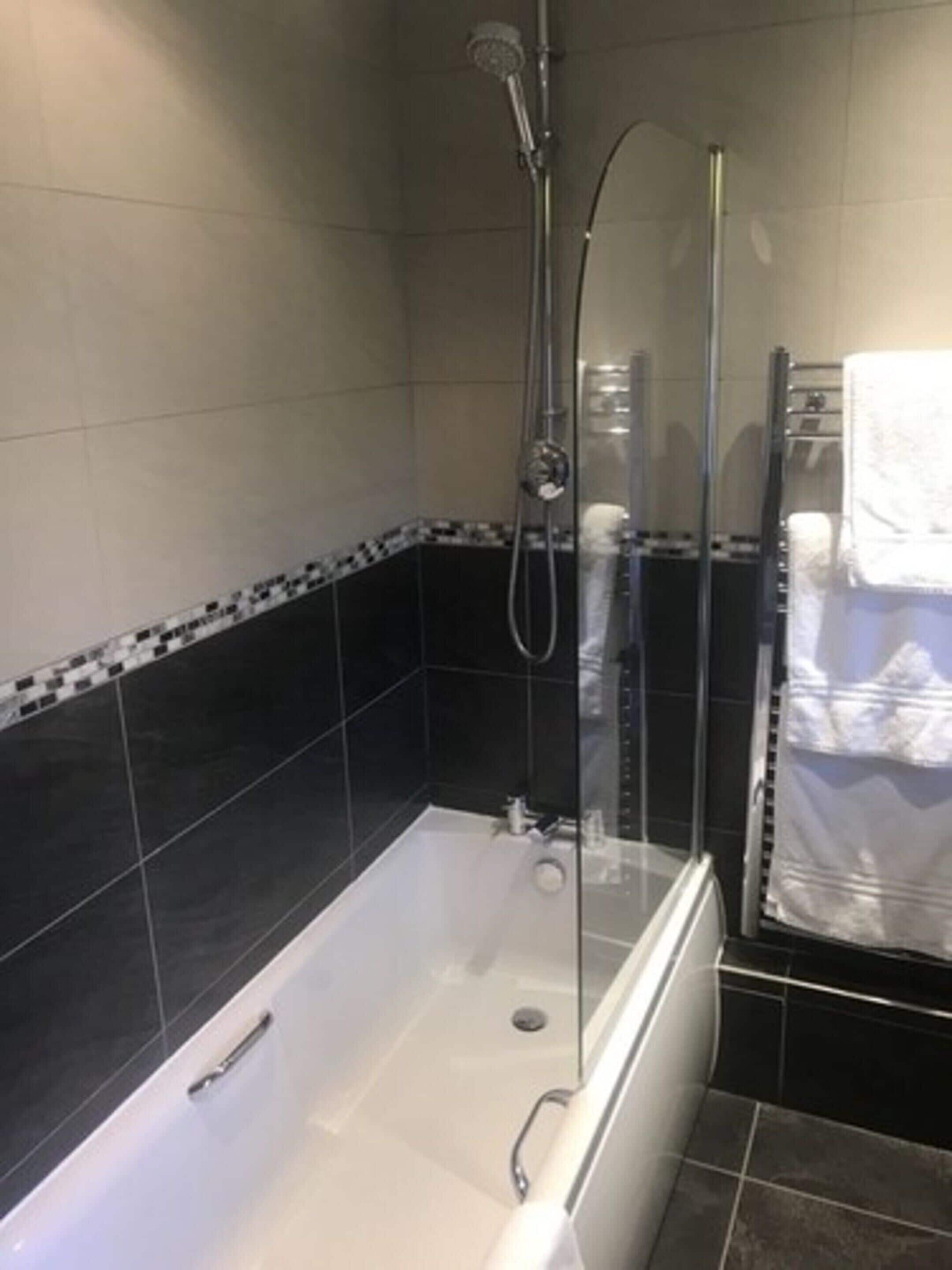Un bagno moderno con doccia vetrata, una vasca da bagno bianca e un rivestimento in piastrelle bianche e nere.