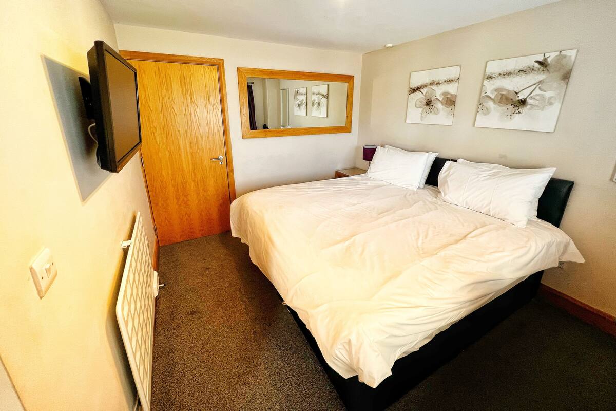 Une chambre d’hôtel avec un lit, un téléviseur fixé au mur, une porte et des œuvres d’art accrochées au mur.