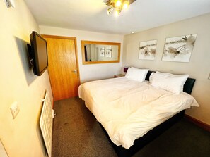 Une chambre d’hôtel avec un lit, un téléviseur fixé au mur, une porte et des œuvres d’art accrochées au mur.