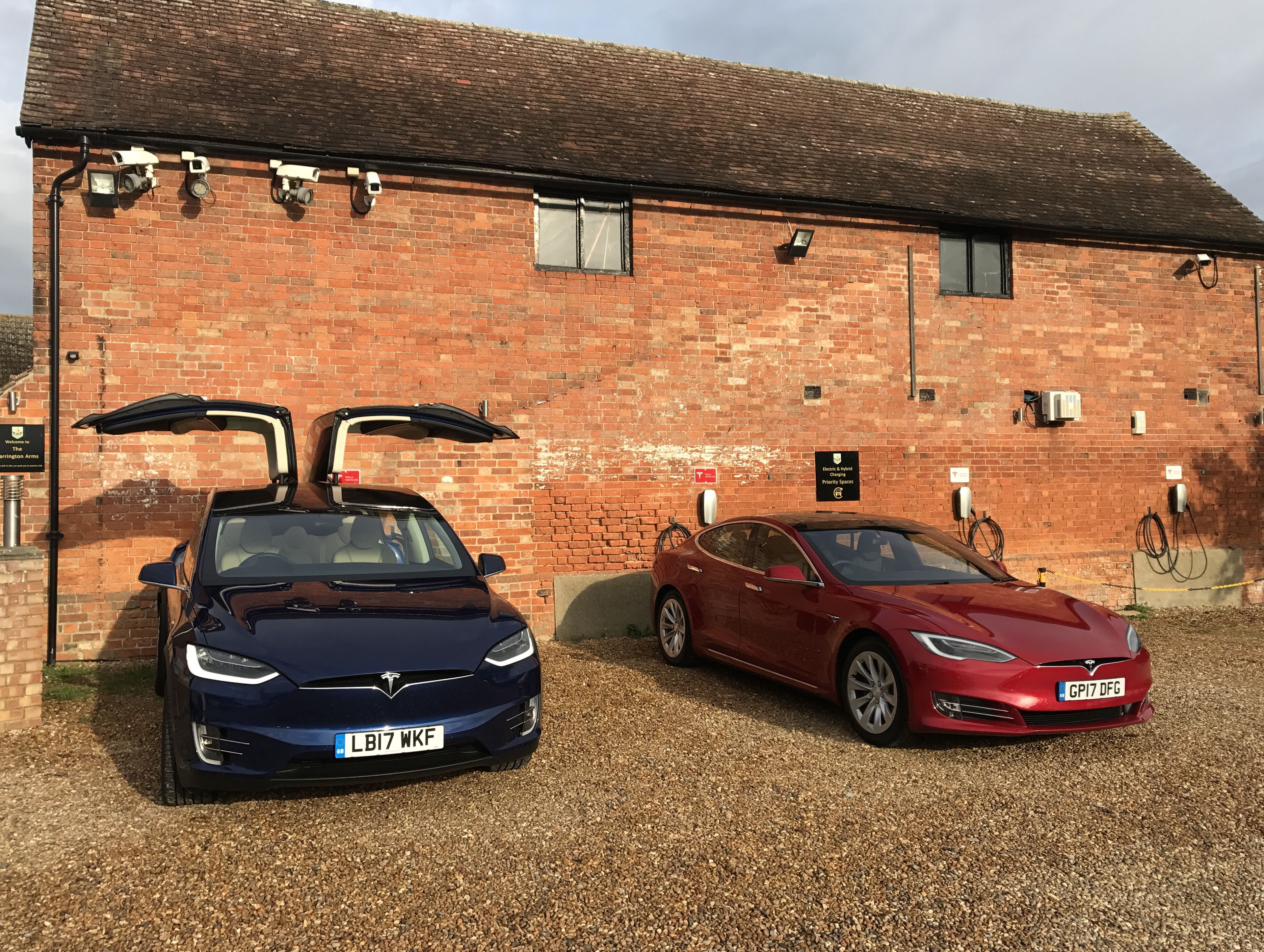 Two cars parked in front of a brick building with solar panels and a sign indicating electric vehicle charging.