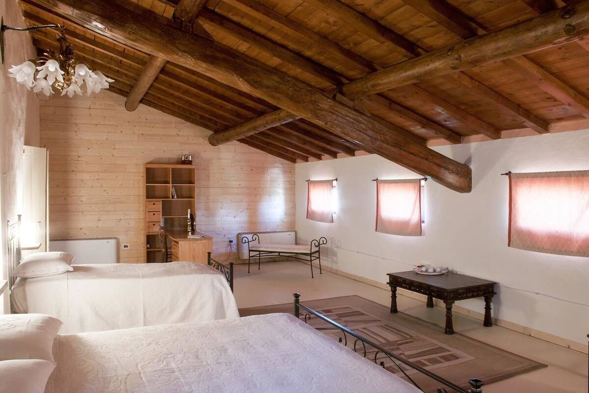 A room with two beds, a wooden ceiling, a small table, and a bench.