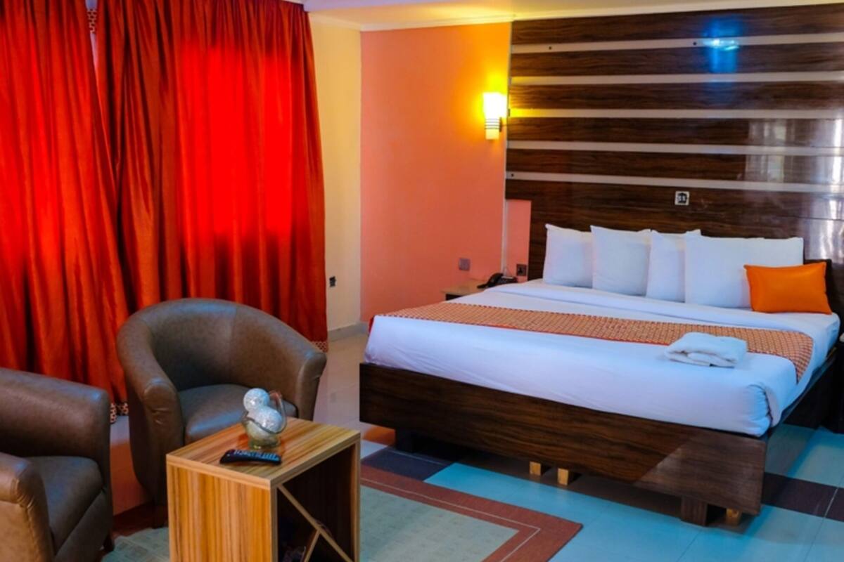 A hotel room with a bed, a chair, a small table, and a red curtain.