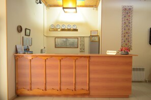 A reception desk with a wooden finish, a clock above it, and a sign labeled "RECEPTION". - Kabir Hotel (Bukhara)
