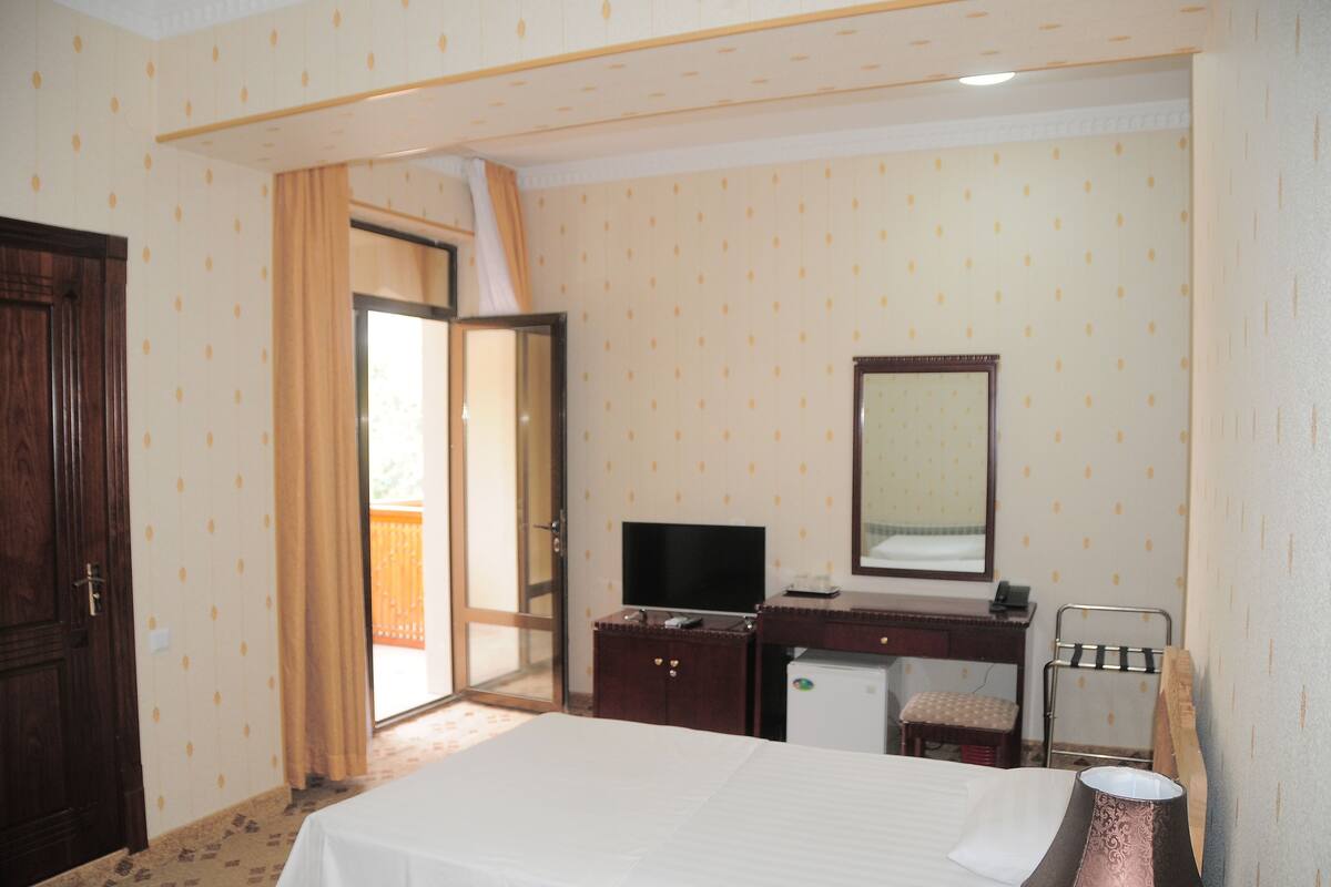 A hotel room with a bed, a desk with a computer, a mirror, a small refrigerator, and a chair.
