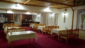 A dining area with wooden tables and benches, a patterned carpet, and a thatched ceiling. - Kabir Hotel (Bukhara)