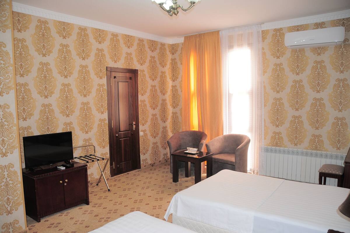 A hotel room with a bed, a TV, a desk, two chairs, and a wardrobe.