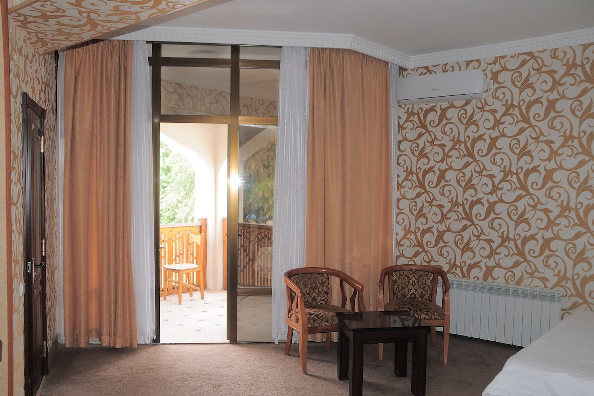A hotel room with a sliding glass door leading to an outdoor area, a wooden table, two chairs, and a radiator.