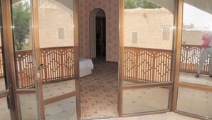 A room with a bed, a wooden partition, and a view of a brick wall outside. - Kabir Hotel (Bukhara)