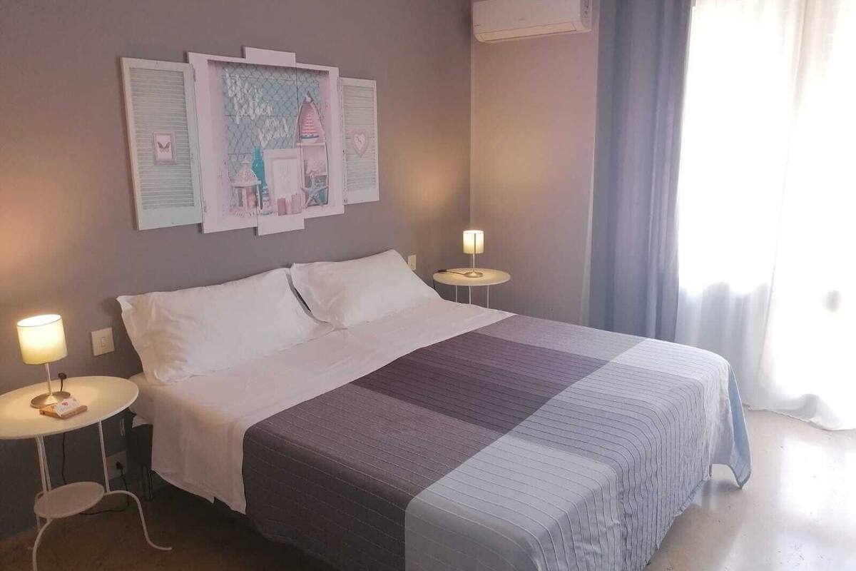 Un letto rifatto con coperta a righe, due comodini con lampade e una parete con quadri.