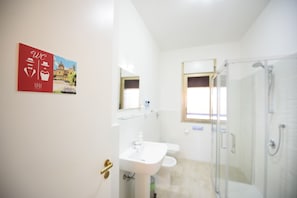 Une salle de bain avec un lavabo, des toilettes et une douche. Il y a une fenêtre donnant sur un immeuble.