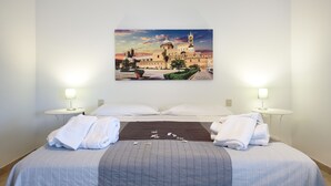 Habitación de hotel con una cama grande, dos mesitas de noche con lámparas, un cuadro de un edificio en la pared y toallas ordenadamente dobladas sobre la cama.
