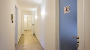 Un pasillo con paredes blancas, una puerta azul y un interruptor de luz en la pared.