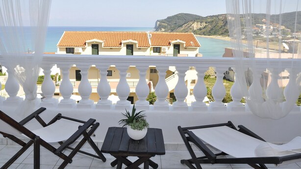 A balcony with white balustrades, a wooden table with a potted plant, and two lounge chairs. - Fedra Mare Apartment (Corfu)