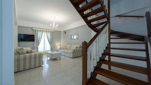 A spacious living room with a wooden staircase, a flat-screen TV mounted on the wall, and a chandelier. - Fedra Mare Apartment (Corfu)