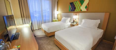 A hotel room with two beds, a desk, a mirror, and a window with curtains.