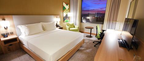 A hotel room with a large bed, a desk, a chair, a TV, and a window with a city view.
