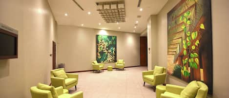 A spacious lobby with a modern design, featuring a seating area with green chairs and a large abstract painting on the wall.