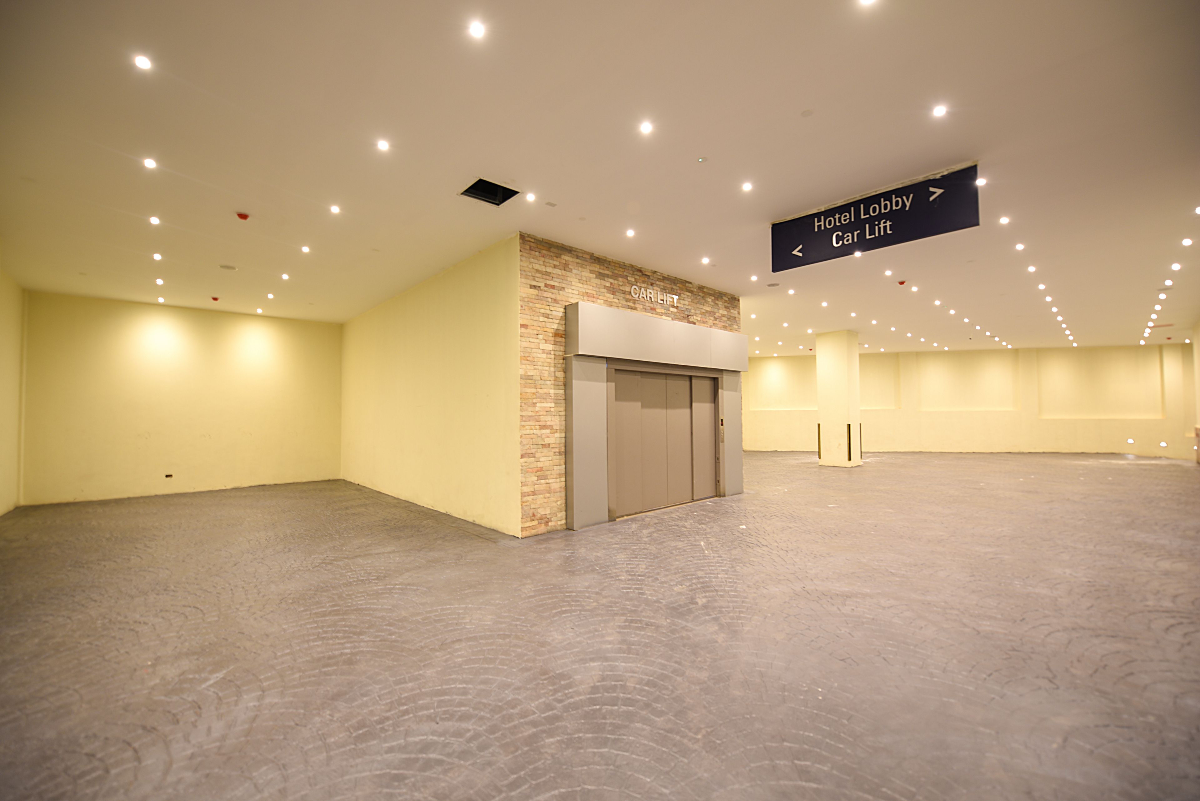 A spacious, well-lit lobby with a car lift and a sign directing to the hotel lobby.