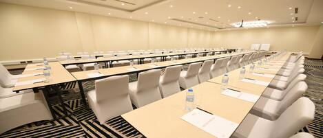 A conference room with long tables, white chairs, water bottles, and name cards.
