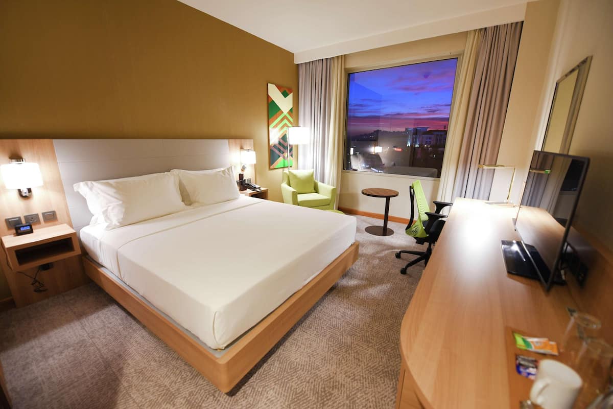 Une chambre d’hôtel avec un grand lit, un bureau, une chaise, une télévision et une fenêtre donnant sur la ville.
