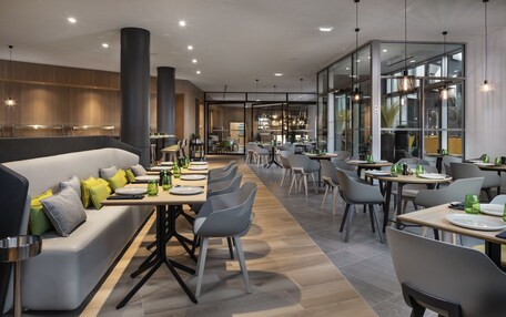 A modern restaurant with a long communal dining table, individual tables, and a seating area with a sofa.