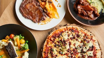 A variety of dishes including steak, roasted vegetables, mashed potatoes, and a pizza.