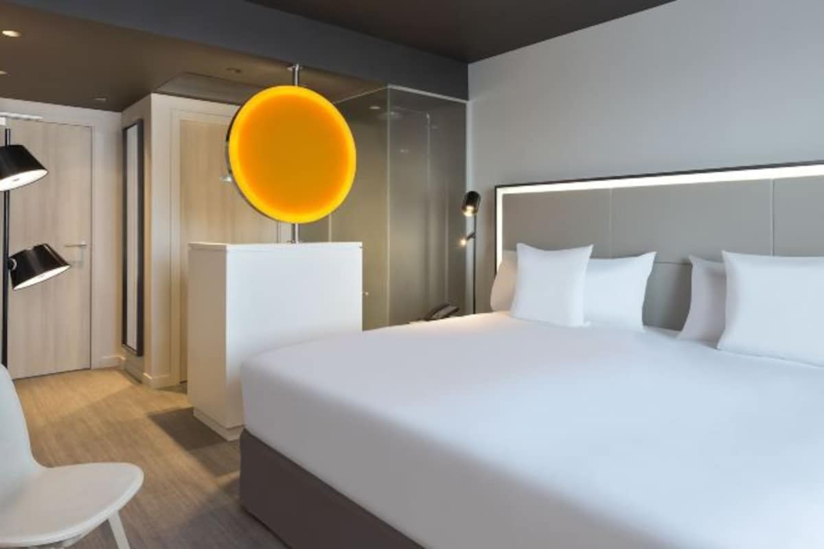 A modern hotel room with a large bed, a round mirror, a desk, and a chair.