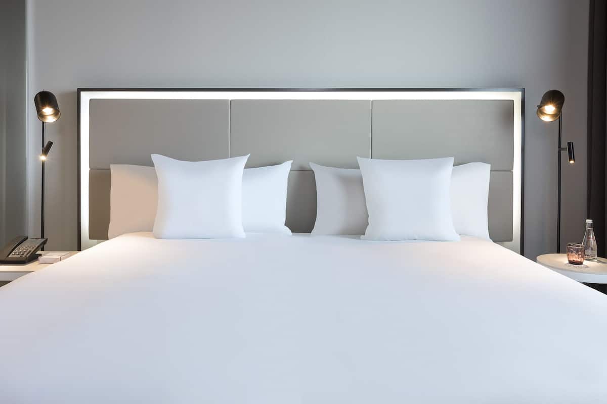 A neatly made bed with white linens and pillows, a bedside table with a lamp, and a bottle on the nightstand.